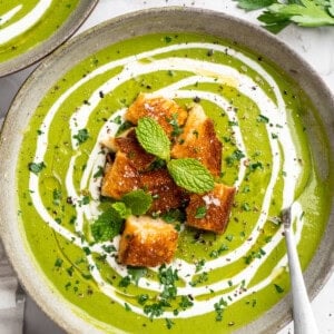 Bowl of broccoli fridge clean-out soup with grilled cheese croutons and swirl of coconut cream.