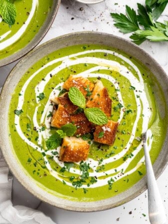 Bowl of broccoli fridge clean-out soup with grilled cheese croutons and swirl of coconut cream.