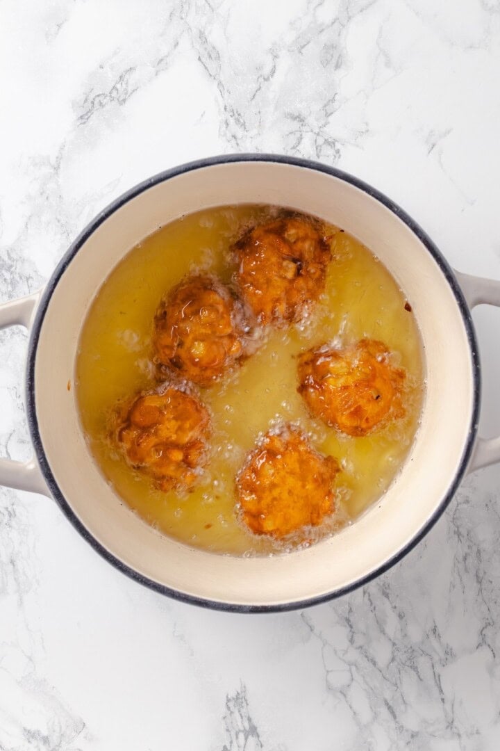 Apple fritters frying in pot of oil.