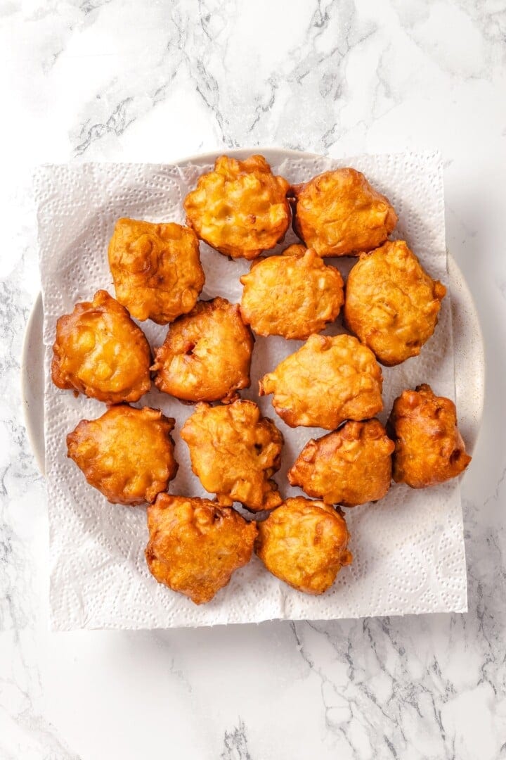 Fried apple fritters on paper towel lined plate.