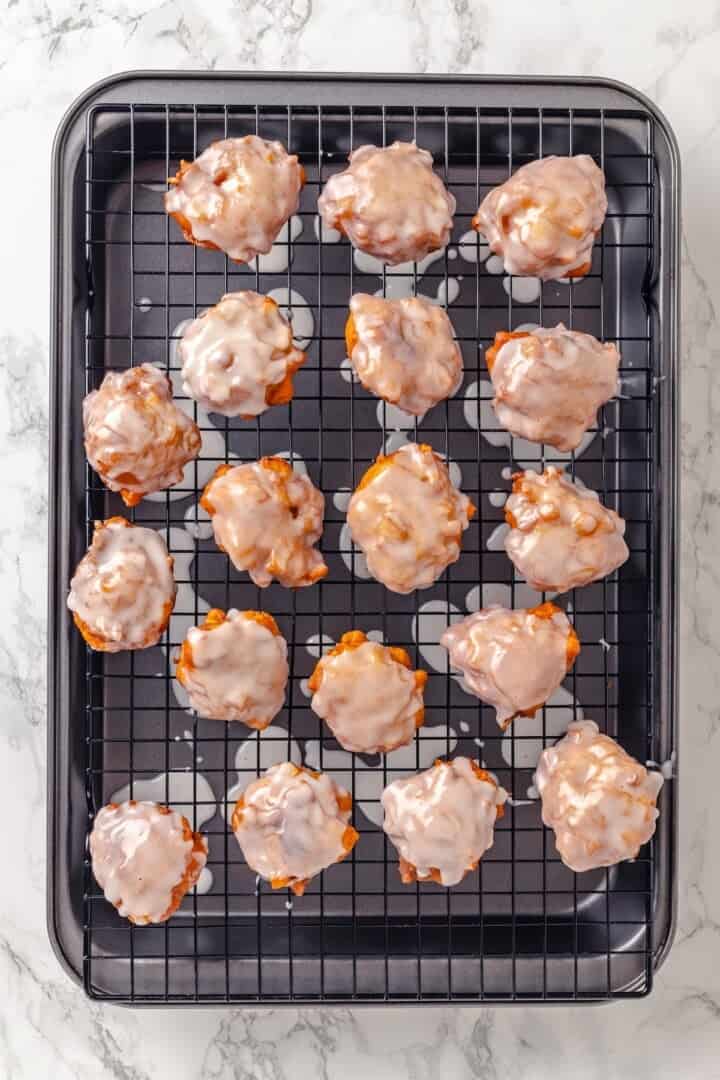 Glazed apple fritters on wire rack set over sheet pan.