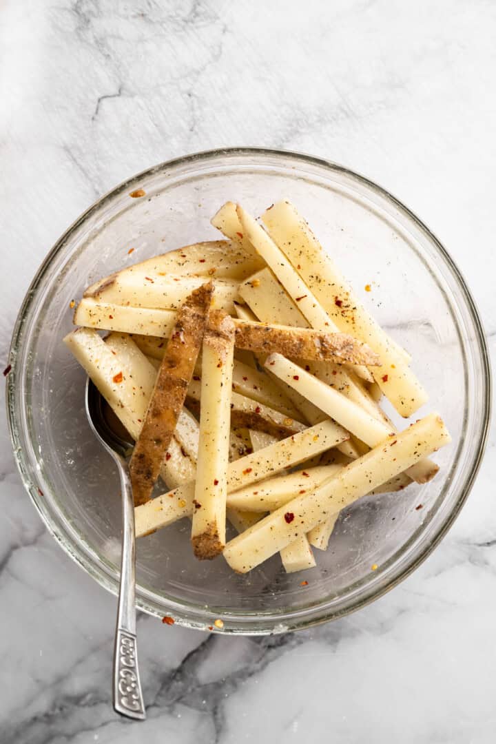 Raw fries in glass bowl with spoon.