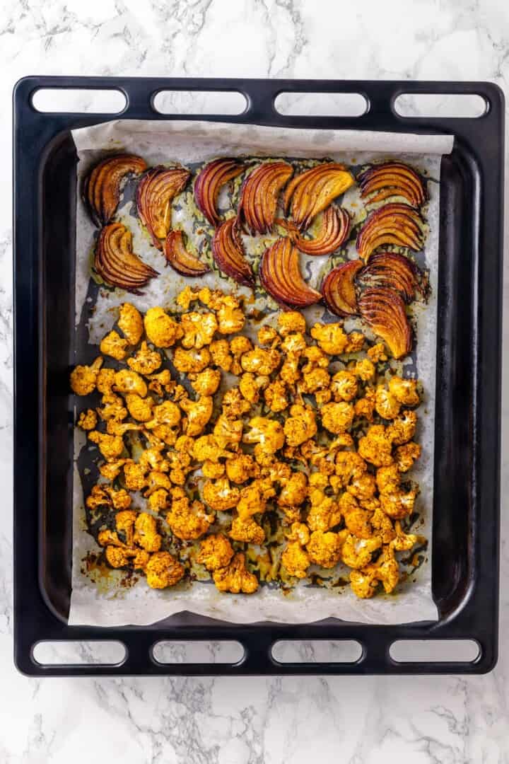 Warm spices mingle with vegetables, golden raisins, olives and chickpeas to make this Moroccan Cauliflower Tagine a delicious vegan dinner! Roasted red onions and cauliflower in pan.