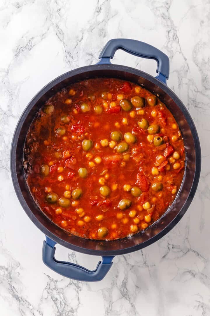 Warm spices mingle with vegetables, golden raisins, olives and chickpeas to make this Moroccan Cauliflower Tagine a delicious vegan dinner! Sauce for Moroccan cauliflower tagine in pan.