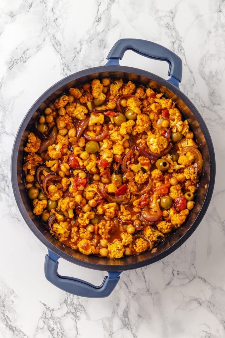 Warm spices mingle with vegetables, golden raisins, olives and chickpeas to make this Moroccan Cauliflower Tagine a delicious vegan dinner! Moroccan cauliflower tagine in skillet.