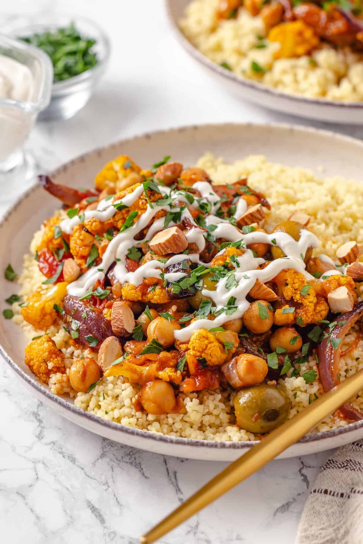 Warm spices mingle with vegetables, golden raisins, olives and chickpeas to make this Moroccan Cauliflower Tagine a delicious vegan dinner! Bowl with Moroccan cauliflower tagine and couscous.
