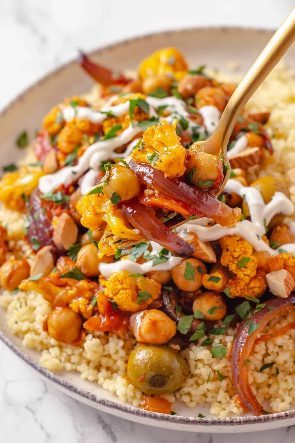 Warm spices mingle with vegetables, golden raisins, olives and chickpeas to make this Moroccan Cauliflower Tagine a delicious vegan dinner! Forkful of Moroccan cauliflower tagine held over bowl.