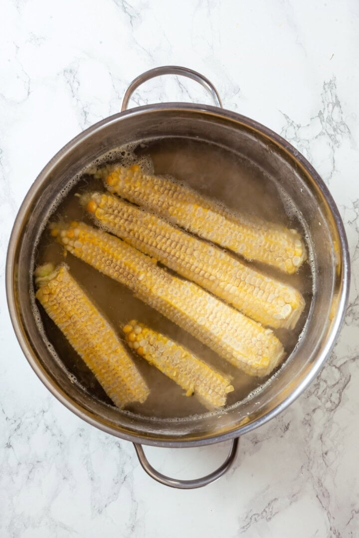 With sweet corn, tender potatoes and a creamy broth, this vegan Corn Chowder recipe is every bit as delicious as the traditional version! Corn cobs simmering in pot of broth.