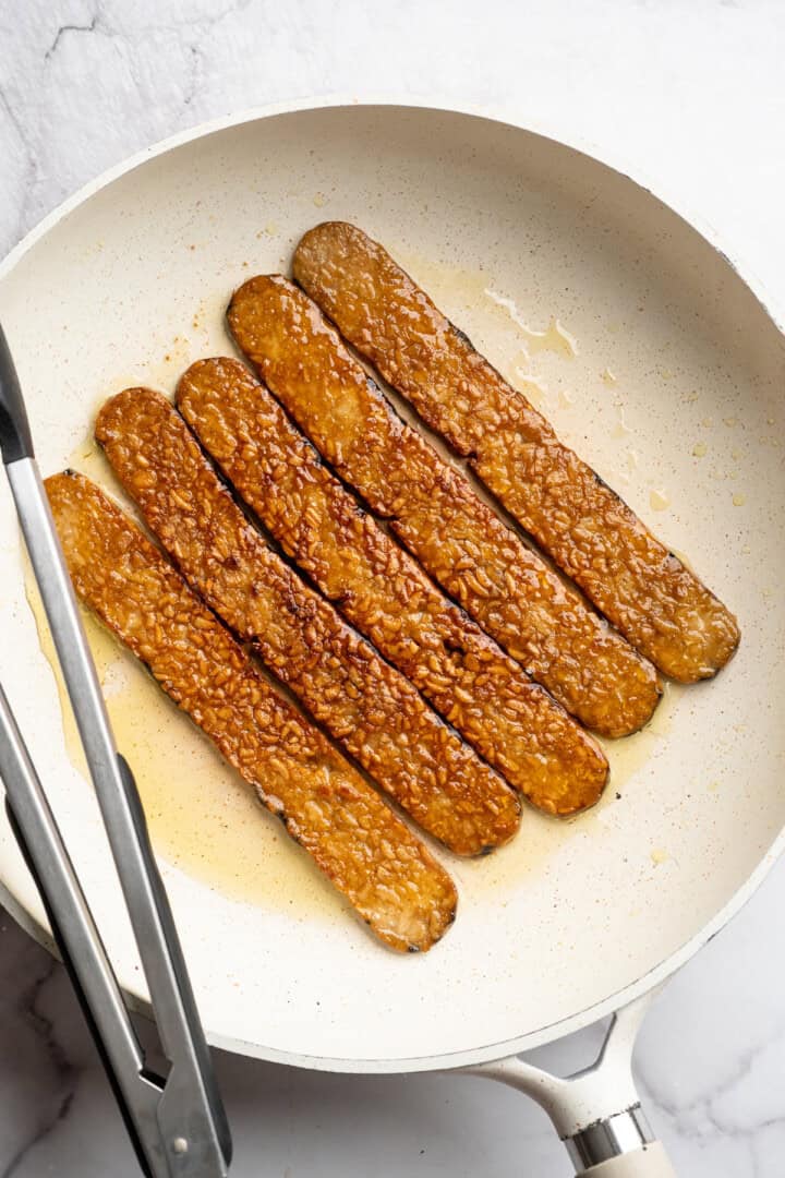 Tempeh bacon cooking in skillet.