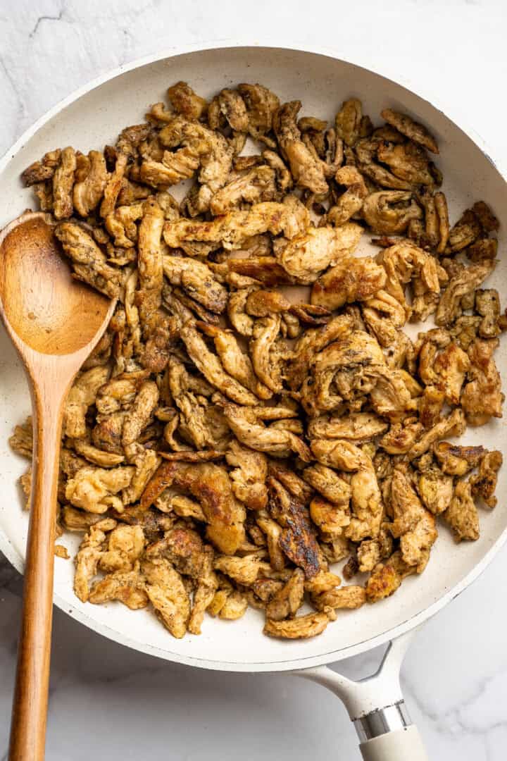 Vegan chicken in skillet with wooden spoon.