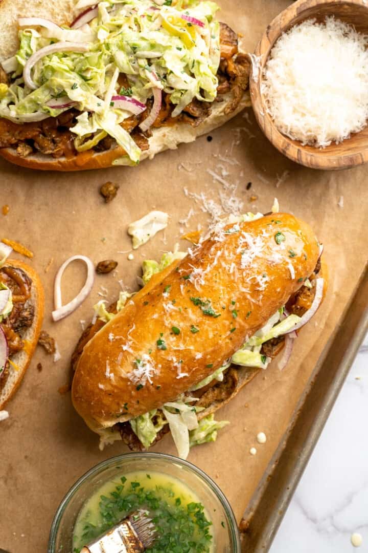 Assembled vegan grinder sandwich with bowl of Parmesan and bowl of herbed butter.
