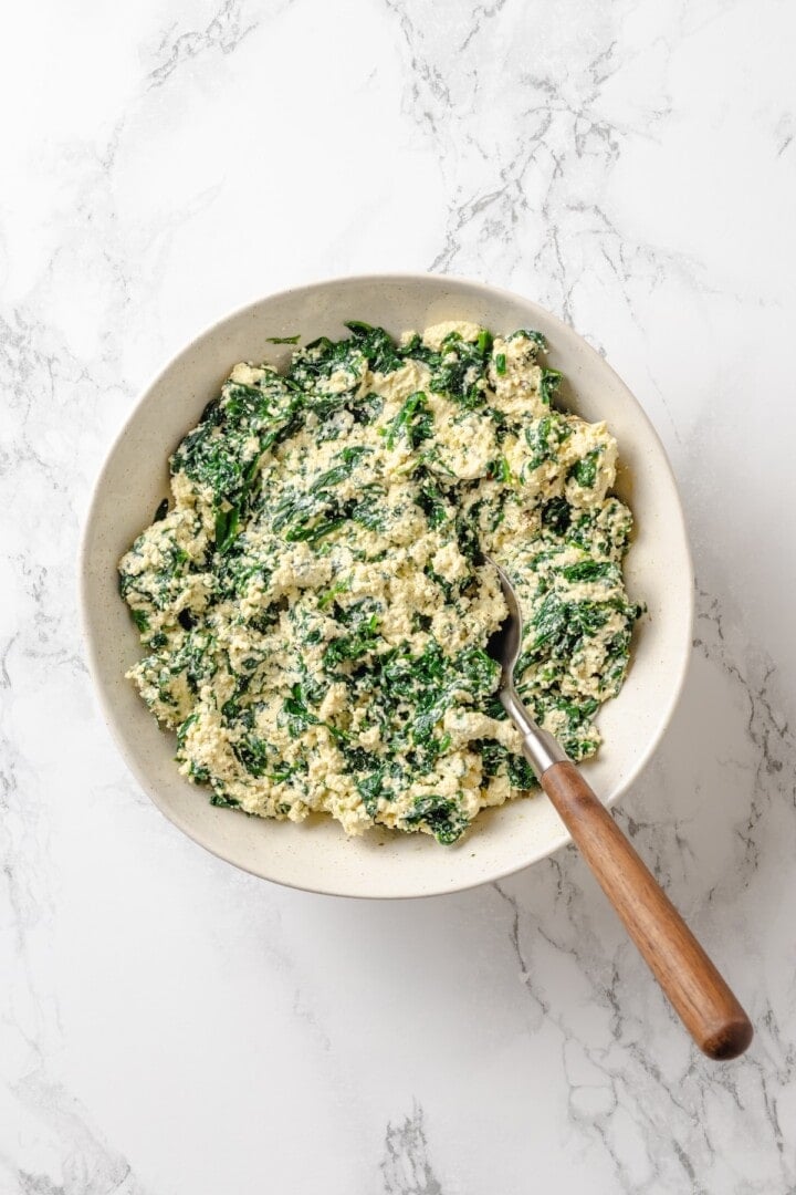 With layers of creamy squash, spinach ricotta and vegan cheese, this butternut squash lasagna is hearty, rich and full of cozy fall flavour! Ricotta and spinach mixture in bowl with spoon.