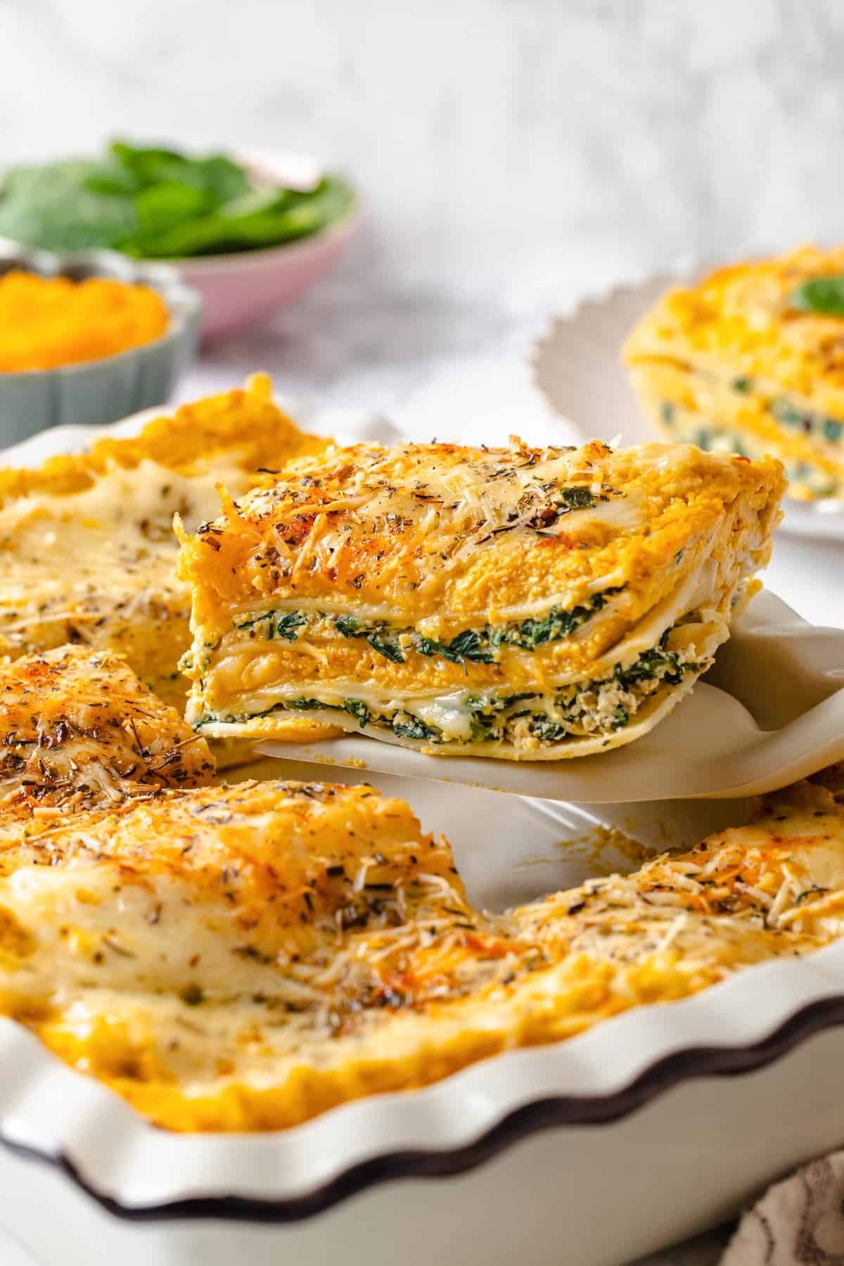 With layers of creamy squash, spinach ricotta and vegan cheese, this butternut squash lasagna is hearty, rich and full of cozy fall flavour! Spatula lifting slice of butternut squash lasagna from casserole dish.