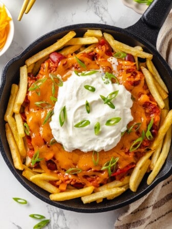 Skillet of vegan chili cheese fries topped with sour cream and green onions.