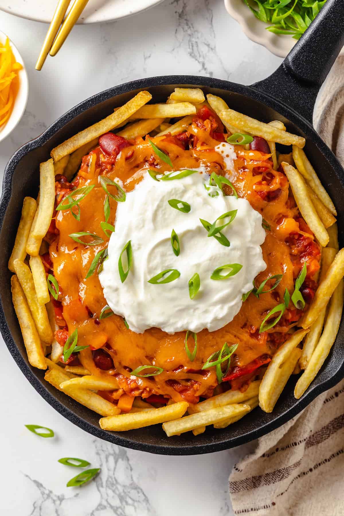 Skillet of vegan chili cheese fries topped with sour cream and green onions.
