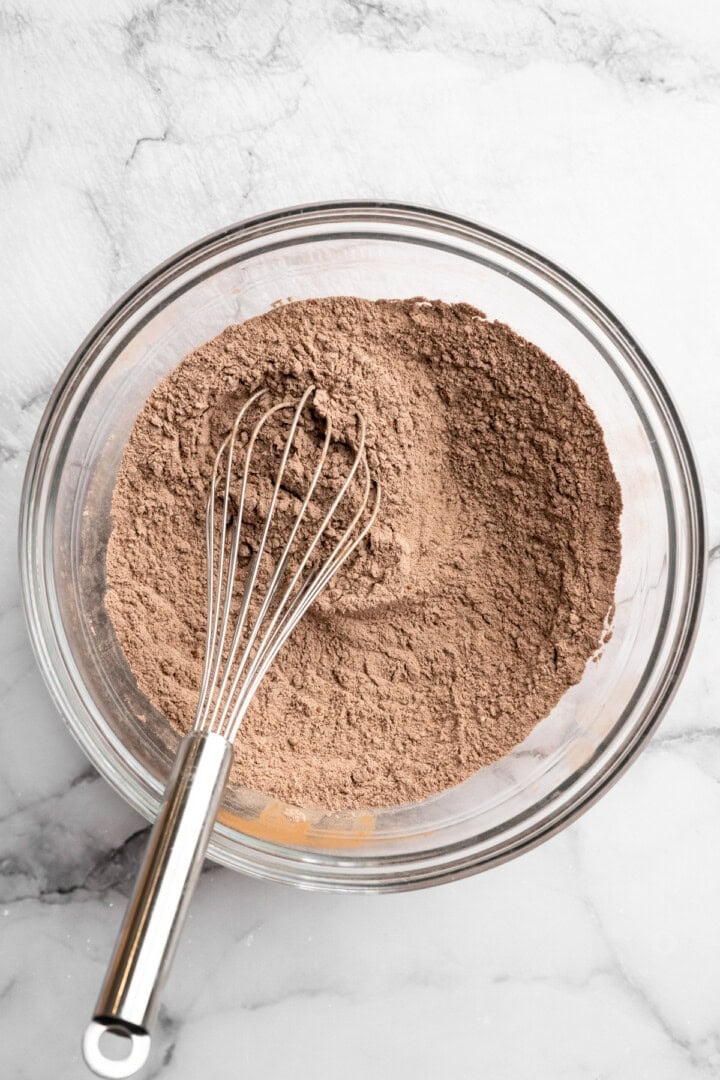 Dry ingredients for chocolate peppermint cookies in glass bowl with whisk.