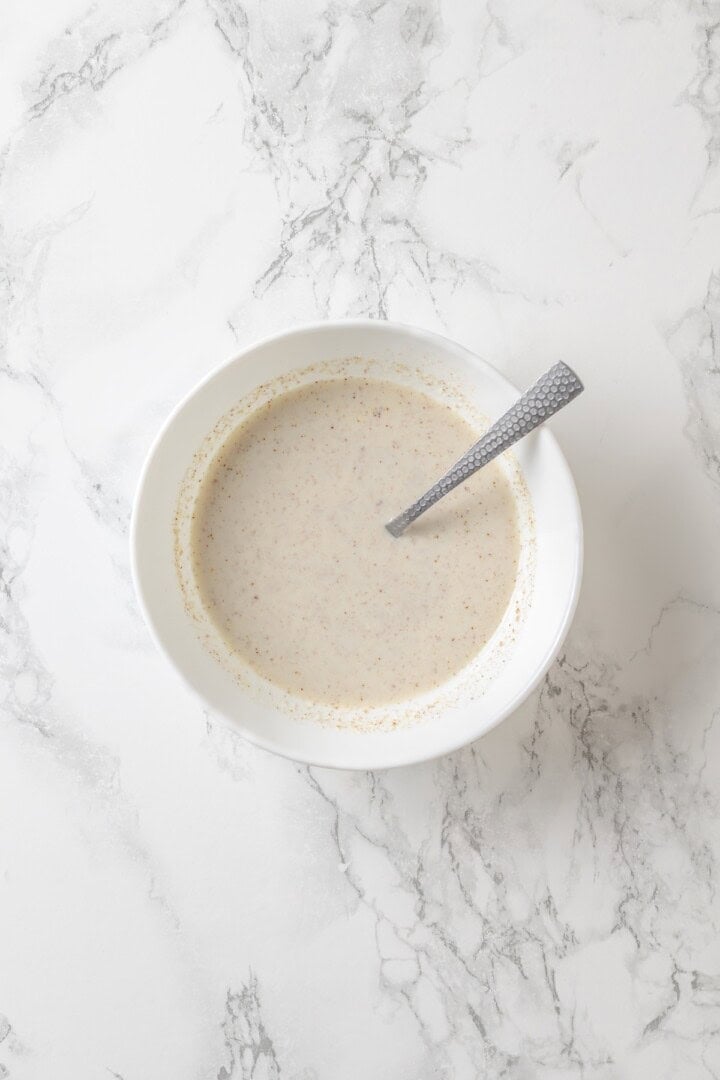 This vegan coffee cake recipe is a bakery-style treat! Moist and tender, with a cinnamon swirl and irresistible crumb topping. Delicious! Flax and milk mixture in bowl with spoon.