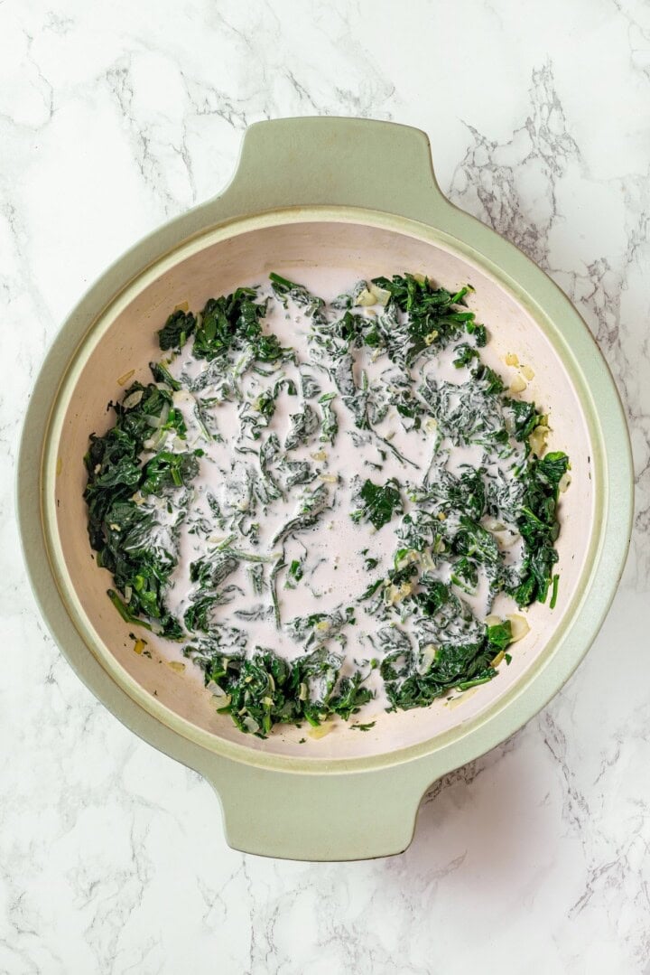 Cashew cream added to spinach in skillet.
