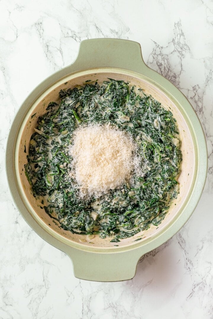 Vegan Parmesan added to creamed spinach in skillet.