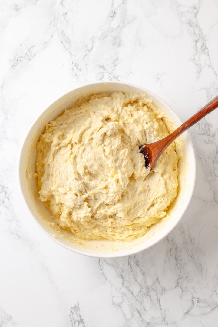 Soft, gooey and sticky, this Vegan Monkey Bread recipe is an irresistible pull-apart treat that's perfect for weekend brunches and holidays! Monkey bread dough in bowl with wooden spoon.