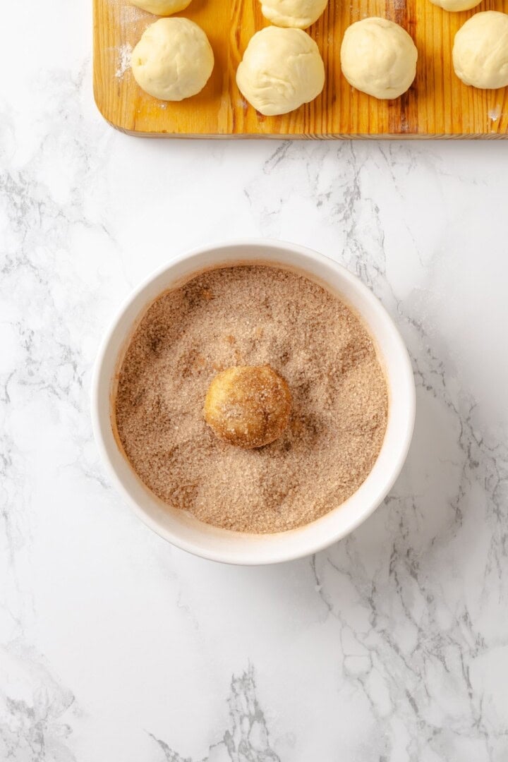 Soft, gooey and sticky, this Vegan Monkey Bread recipe is an irresistible pull-apart treat that's perfect for weekend brunches and holidays! Dipping ball of dough in cinnamon sugar.