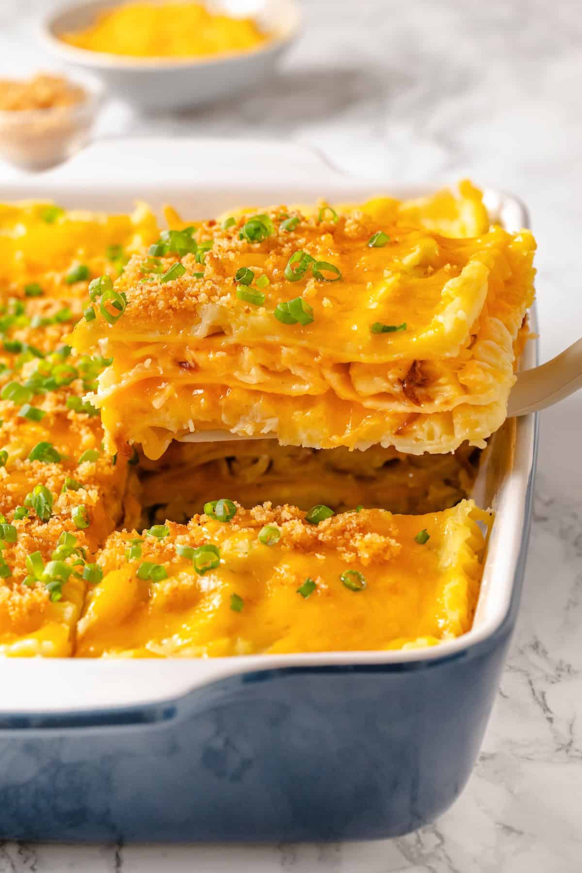 This vegan pierogi casserole layers a cheesy potato filling with lasagna noodles for pierogi vibes without the work of making dumplings! Spatula lifting slice of pierogi casserole from dish.