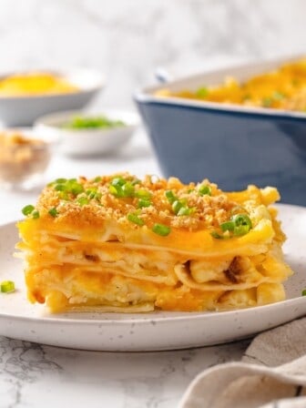 Slice of pierogi casserole on plate with green onions for garnish.