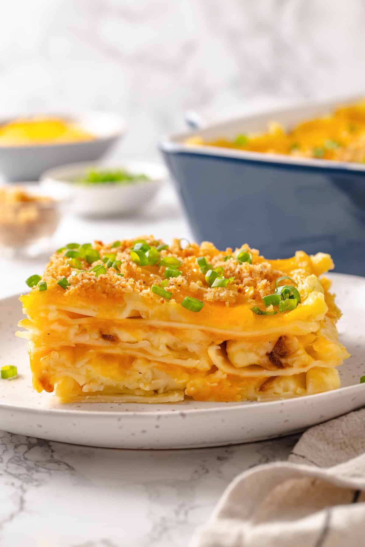 This vegan pierogi casserole layers a cheesy potato filling with lasagna noodles for pierogi vibes without the work of making dumplings! Slice of pierogi casserole on plate with green onions for garnish.