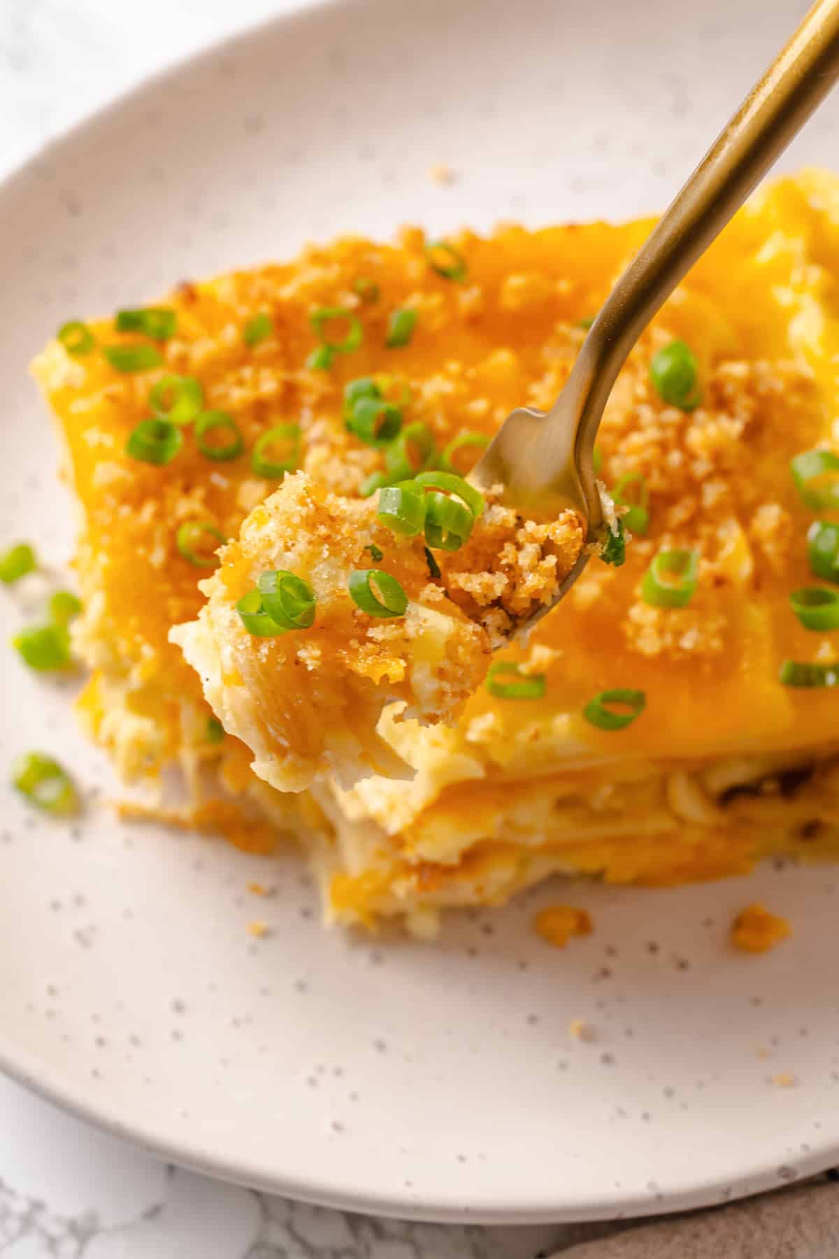 This vegan pierogi casserole layers a cheesy potato filling with lasagna noodles for pierogi vibes without the work of making dumplings! Forkful of pierogi casserole held over plate.