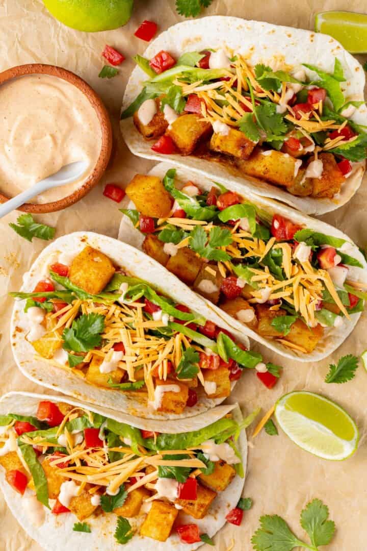 These copycat Taco Bell vegan spicy potato soft tacos are even better than the original. Crispy potatoes and creamy sauce make them so tasty! 4 spicy potato soft tacos with bowl of creamy spicy sauce.