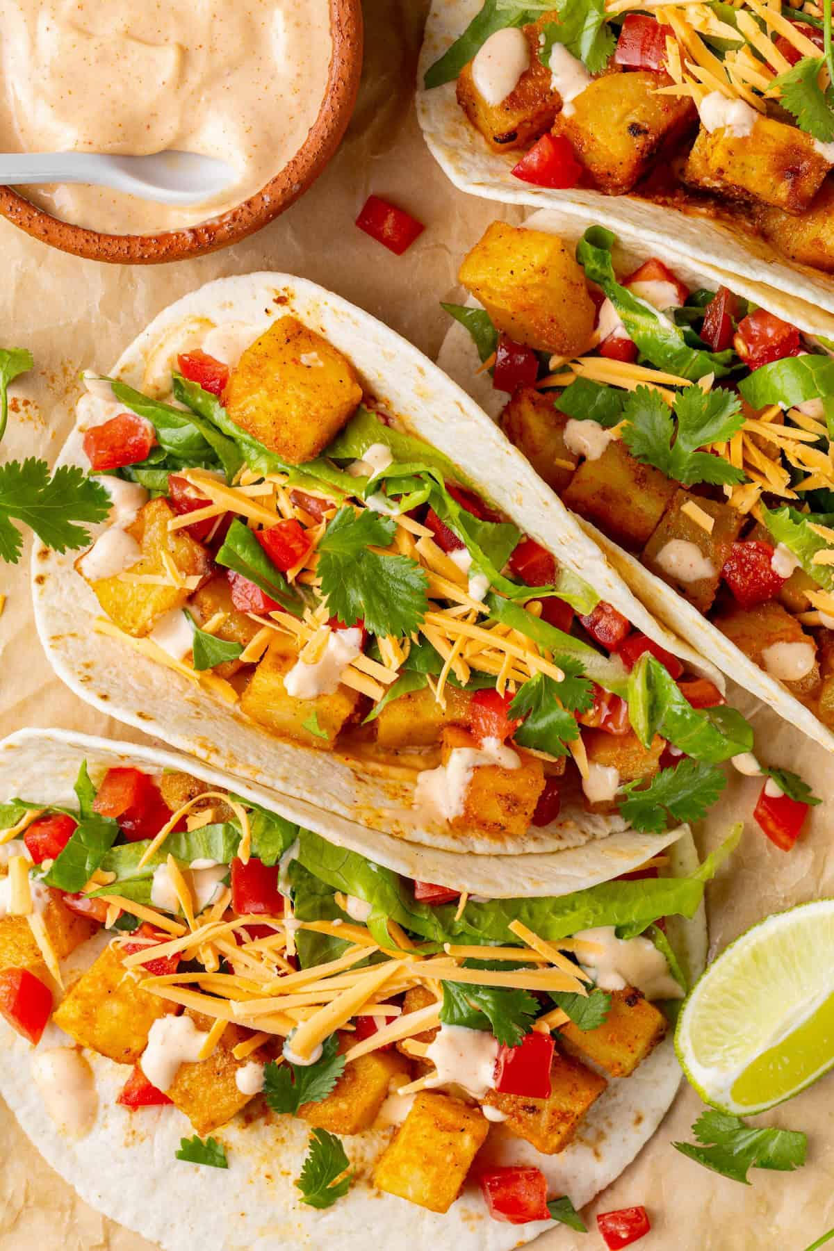 These copycat Taco Bell vegan spicy potato soft tacos are even better than the original. Crispy potatoes and creamy sauce make them so tasty! 4 spicy potato soft tacos with bowl of spicy cream sauce.