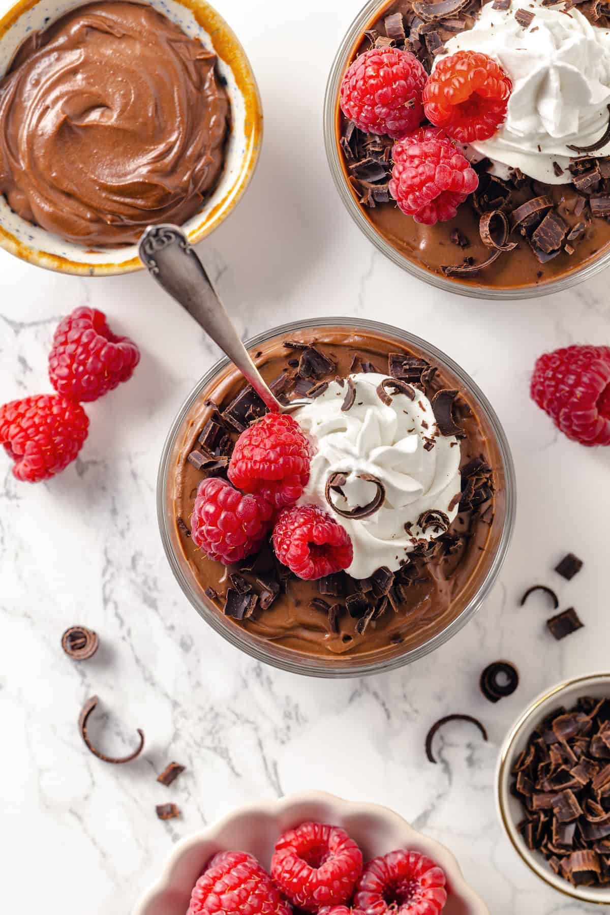 Silken Tofu Chocolate Mousse is the easiest vegan dessert you'll ever make! It's rich and indulgent, with a velvety smooth texture. So good! Two bowls of vegan chocolate mousse with whipped cream, raspberries, and chocolate shavings.