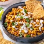 Bowl of Mexican street corn dip with two tortilla chips.