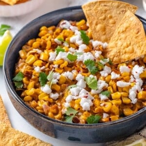 Bowl of Mexican street corn dip with two tortilla chips.