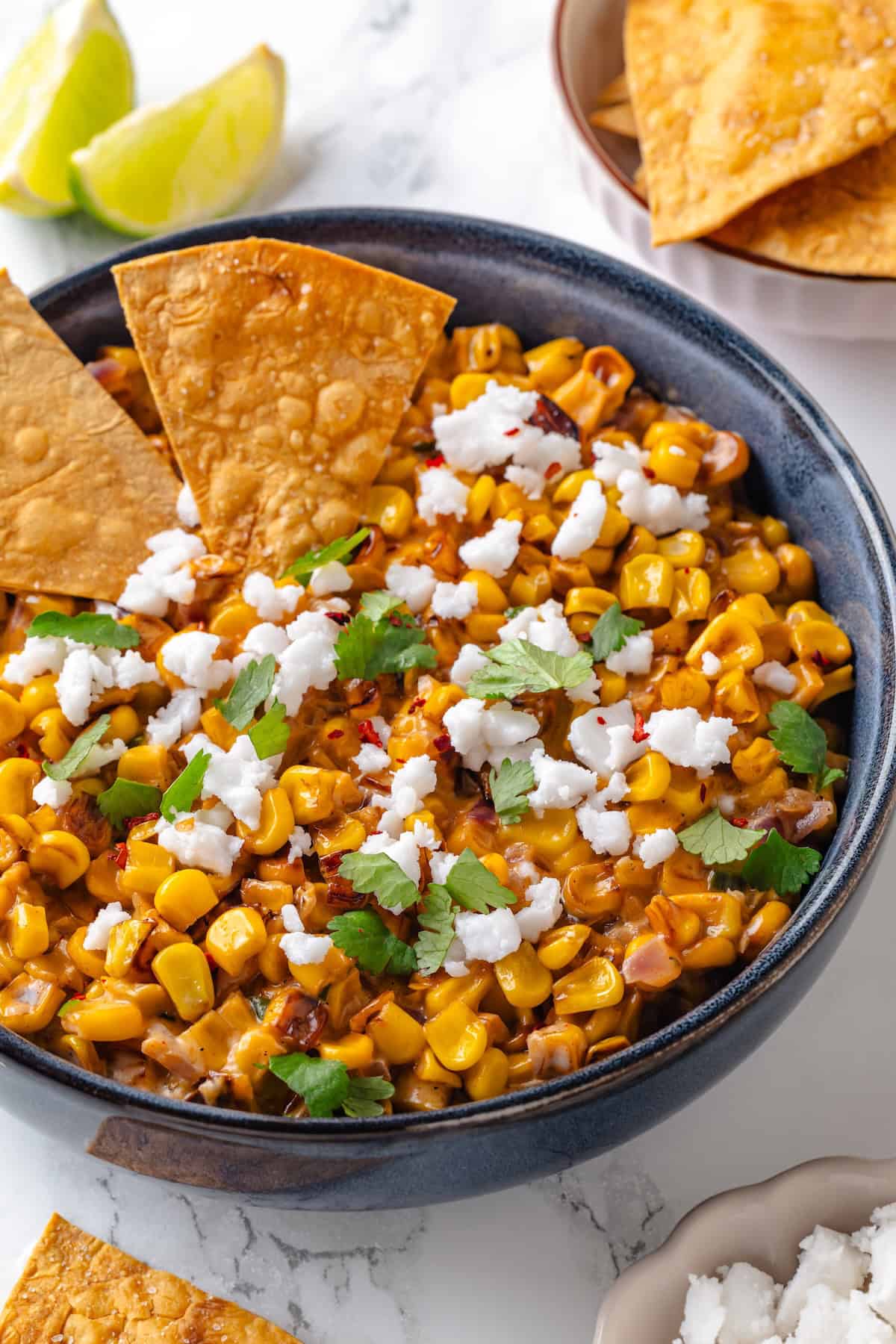 This vegan Mexican Street Corn Dip is creamy, smoky, and a little bit spicy (just like elotes!) for an easy appetizer everyone will love! Two tortilla chips in bowl of Mexican street corn dip.