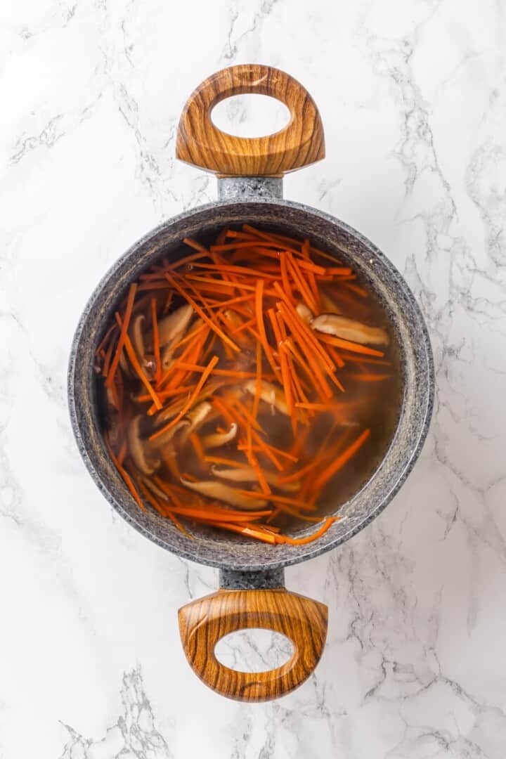 This cozy Miso Tofu Soup recipe is made with wakame, ginger, carrots and homemade dashi for a light, nourishing and flavorful vegan soup. Carrots and shiitake mushrooms in pot of dashi.