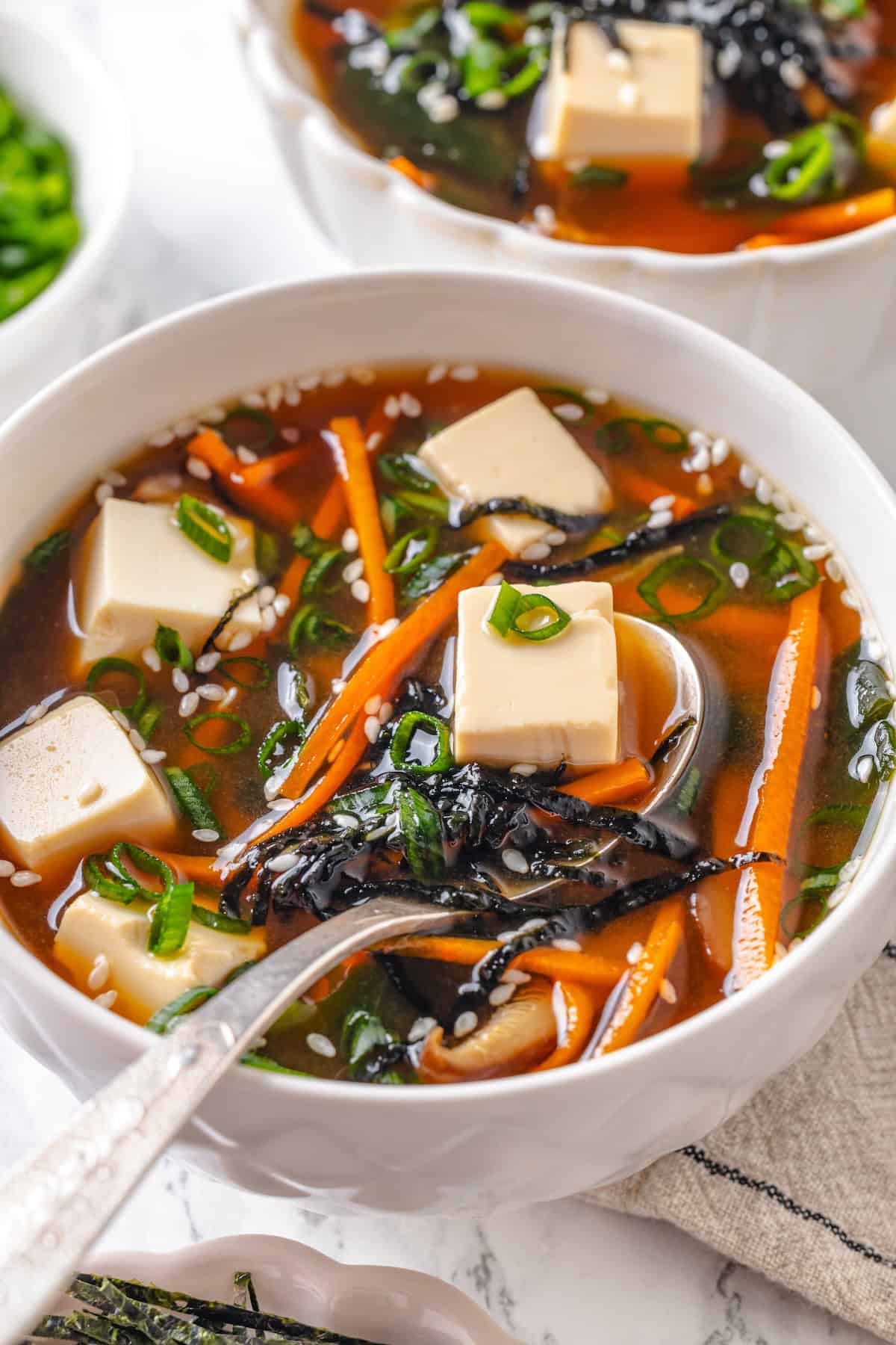 This cozy Miso Tofu Soup recipe is made with wakame, ginger, carrots and homemade dashi for a light, nourishing and flavorful vegan soup. Spoonful of vegan miso tofu soup in bowl.