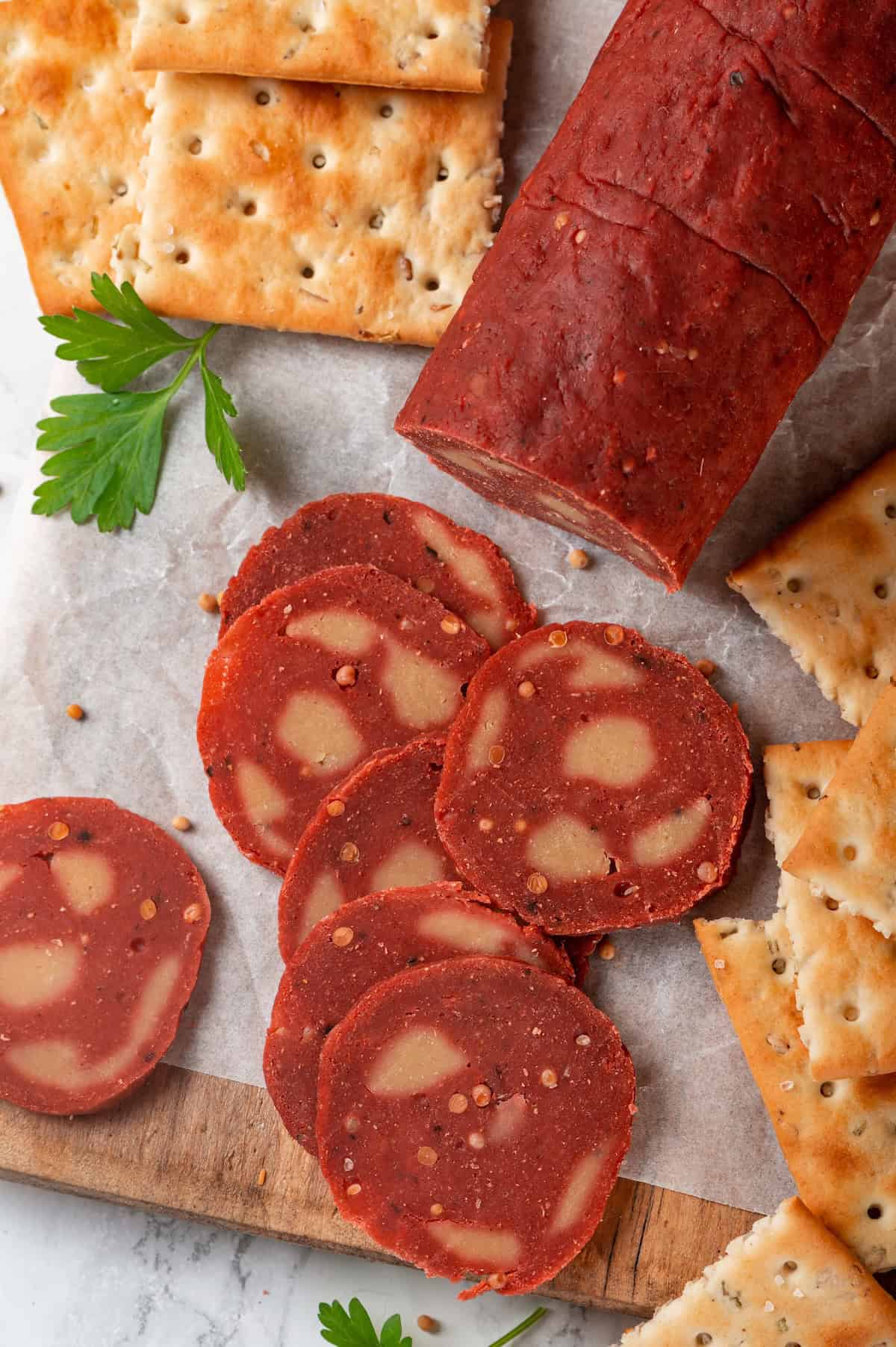 This easy vegan salami recipe is smoky, savoury and sliceable, just like the real deal! Perfect for sandwiches and charcuterie boards. Vegan salami slices spread on board with crackers.