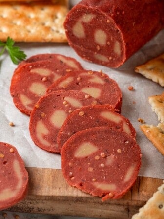 Slices of vegan salami on parchment lined wooden board.