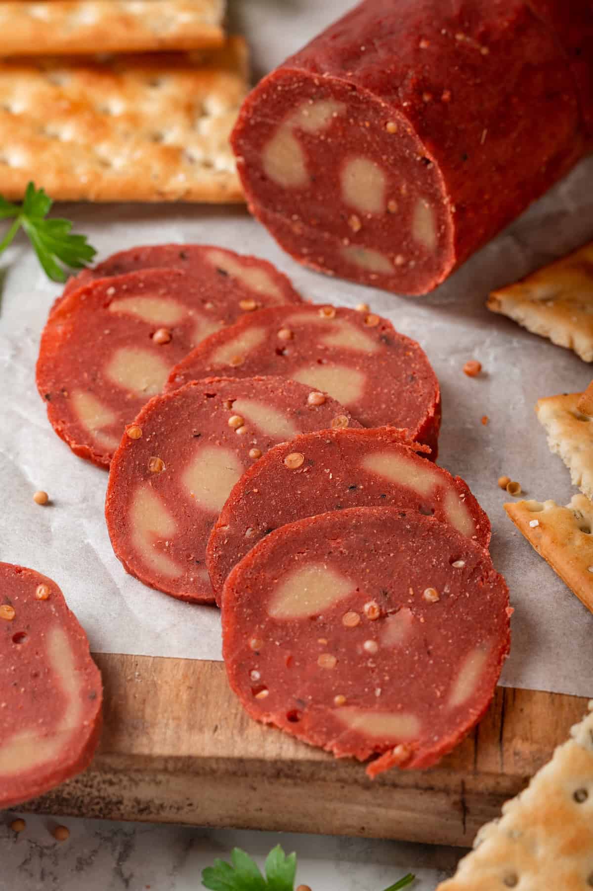 This easy vegan salami recipe is smoky, savoury and sliceable, just like the real deal! Perfect for sandwiches and charcuterie boards. Slices of vegan salami on parchment lined wooden board.