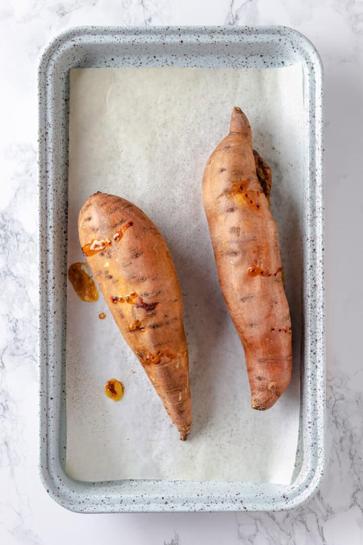 This soft, pillowy homemade sweet potato gnocchi is tossed with rosemary garlic butter and walnuts for a restaurant-style vegan dinner! Two roasted sweet potatoes on sheet pan.