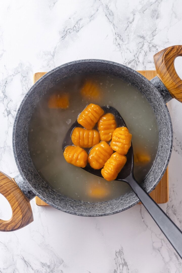 This soft, pillowy homemade sweet potato gnocchi is tossed with rosemary garlic butter and walnuts for a restaurant-style vegan dinner! Slotted spoon removing sweet potato gnocchi from boiling water.