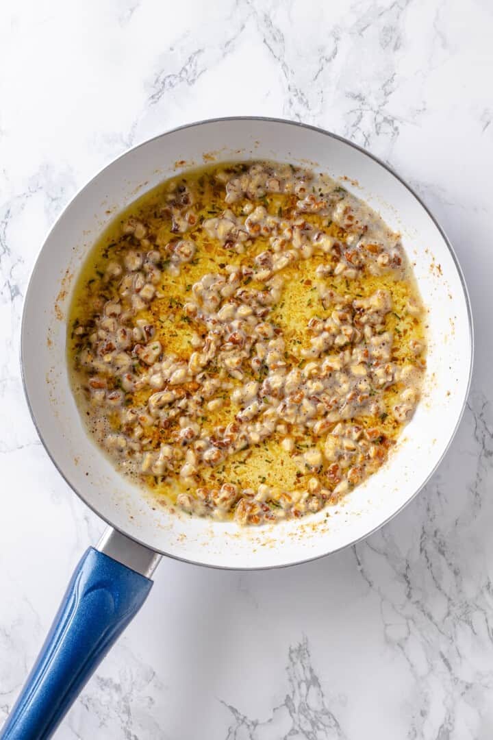 This soft, pillowy homemade sweet potato gnocchi is tossed with rosemary garlic butter and walnuts for a restaurant-style vegan dinner! Garlic butter sauce in skillet with walnuts.