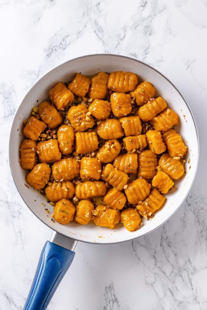 This soft, pillowy homemade sweet potato gnocchi is tossed with rosemary garlic butter and walnuts for a restaurant-style vegan dinner! Sweet potato gnocchi in skillet with butter sauce.
