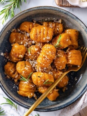 Fork in bowl of sweet potato gnocchi with vegan Parmesan and rosemary.