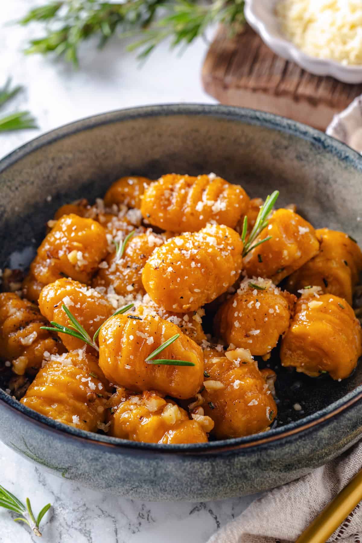 This soft, pillowy homemade sweet potato gnocchi is tossed with rosemary garlic butter and walnuts for a restaurant-style vegan dinner! Bowl of vegan sweet potato gnocchi with rosemary garlic butter sauce.