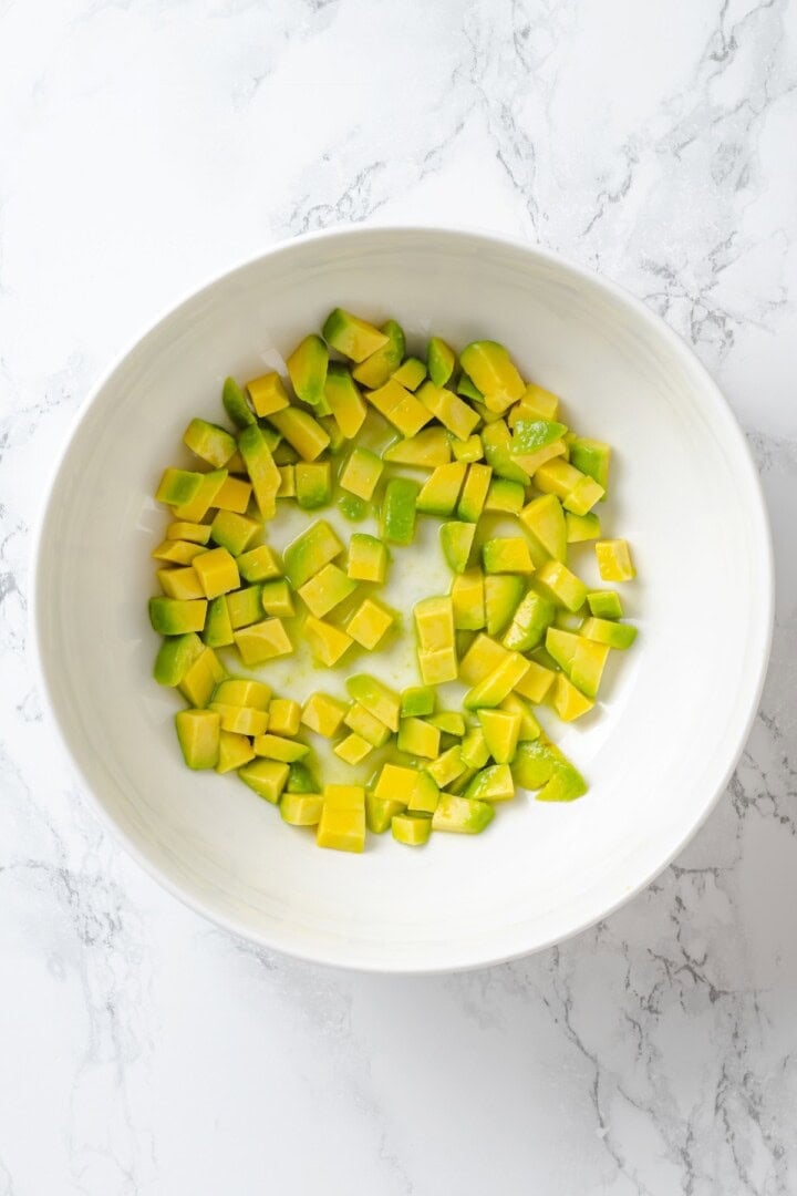 This cowboy caviar recipe is made with black-eyed peas, black beans, avocado, veggies, and a zesty dressing. Use it as a dip or a side dish! Avocado cubes in bowl.