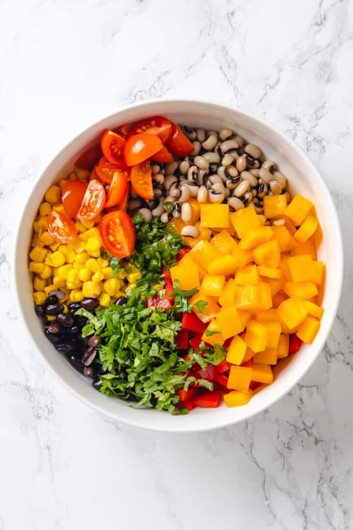 This cowboy caviar recipe is made with black-eyed peas, black beans, avocado, veggies, and a zesty dressing. Use it as a dip or a side dish! Bowl with black eyed peas, bell peppers, cilantro, black beans, corn, and tomatoes.