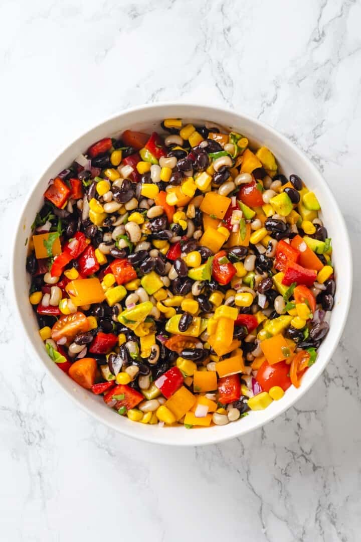 This cowboy caviar recipe is made with black-eyed peas, black beans, avocado, veggies, and a zesty dressing. Use it as a dip or a side dish! Bowl of cowboy caviar.