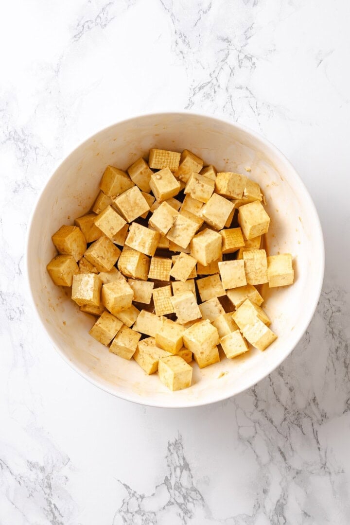 This crispy kung pao tofu is made with bell peppers, crunchy peanuts and a sweet-spicy sauce for a dinner that's even better than takeout! Seasoned tofu cubes in bowl.